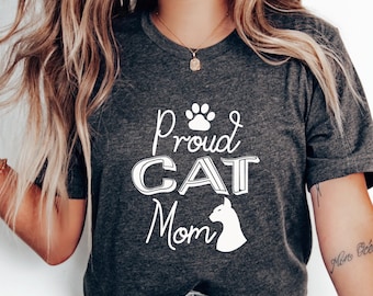 May include: A gray t-shirt with the text "Proud Cat Mom" in white lettering. A white paw print and a white silhouette of a cat's head are also on the shirt.