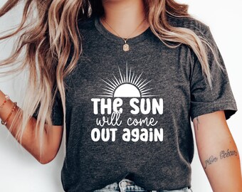 May include: A dark gray t-shirt with a white graphic of a sun with rays and the text "THE SUN will come OUT again".