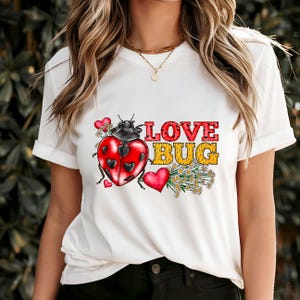 Könnte beinhalten: Weißes T-Shirt mit einer roten und schwarzen Marienkäfergrafik und dem Text "LOVE BUG" in roten und gelben Buchstaben. Der Marienkäfer ist von roten Herzen und weißen Gänseblümchen umgeben.