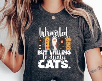 May include: A grey t-shirt with the text "Introverted but willing to discuss cats." The text is in white and is surrounded by five colourful cat paw prints.