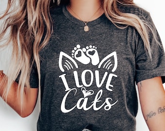 Peut inclure: Un t-shirt gris avec un motif blanc qui dit "J'aime les chats" avec un visage de chat et des empreintes de pattes.
