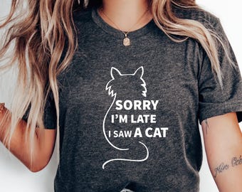 May include: A dark gray t-shirt with a white outline of a cat and the text "Sorry I'm Late I Saw A Cat".