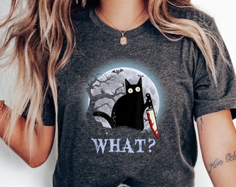 May include: A dark gray t-shirt with a black cat holding a bloody knife in front of a full moon. The cat has large, white eyes. The text "WHAT?" is printed below the cat.