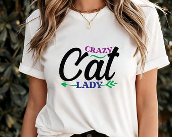 May include: White t-shirt with the text "Crazy Cat Lady" in black, purple, and green. The word "Cat" is in a large, stylized font. The shirt has short sleeves and a crew neck.