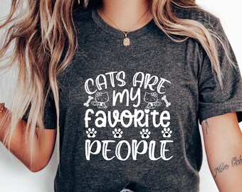 May include: A gray t-shirt with the text "Cats are my favorite people" in white. The text is surrounded by two cartoon cats, two bone icons, and five paw print icons.