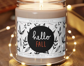 Könnte beinhalten: Eine braune Sojawachskerze mit einem weißen Etikett, auf dem "FIR & FIG CANDLE CO." und "hello FALL" in einem schwarzen Kreis mit weißen Blättern steht. Die Kerze ist 9 oz schwer und handgefertigt in den USA.