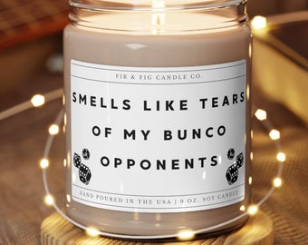 May include: A brown soy candle with a white label that reads "Smells Like Tears of My Bunco Opponents." The label also includes the company name "Fir & Fig Candle Co." and the text "Hand Poured in the USA | 9 oz. Soy Candle."
