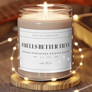 Könnte beinhalten: Eine braune Kerze in einem durchsichtigen Glasgefäß mit einem weißen Etikett, auf dem "FIR & FIG CANDLE CO. SMELLS BETTER THAN GERMAN WIREHAIRED POINTER BREATH Est. 2023 made with love" steht.