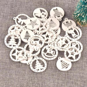 May include: A selection of white Christmas tree decorations featuring cut-out designs of stars, trees, and rocking horses. Each circular ornament has a small hole for hanging. The decorations are arranged on a grey, textured surface.