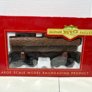 May include: A model railway wagon carrying simulated logs, packaged in a red box. The box features the text "The Original Bachmann Big Haulers" and "Large Scale Model Railroading Product."