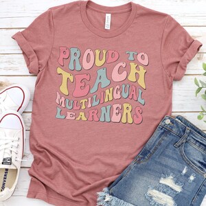 May include: A pink t-shirt with the text "Proud to Teach Multilingual Learners" in a retro font with colorful letters.