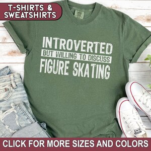 K&ouml;nnte beinhalten: Ein gr&uuml;nes T-Shirt mit wei&szlig;em Text, der "Introvertiert, aber bereit, &uuml;ber Eiskunstlauf zu diskutieren" lautet.