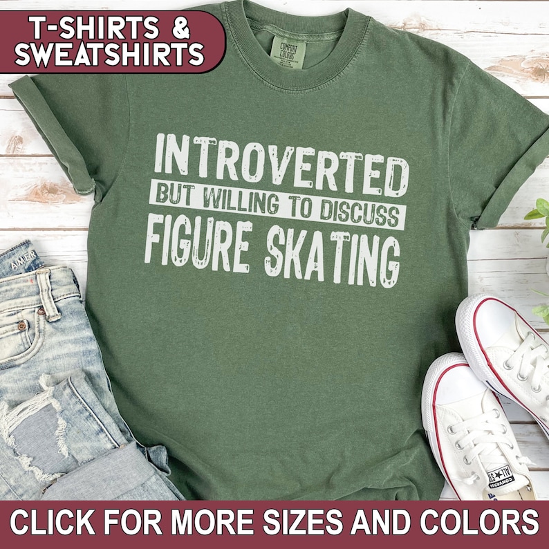 K&ouml;nnte beinhalten: Ein gr&uuml;nes T-Shirt mit wei&szlig;em Text, der "Introvertiert, aber bereit, &uuml;ber Eiskunstlauf zu diskutieren" lautet.