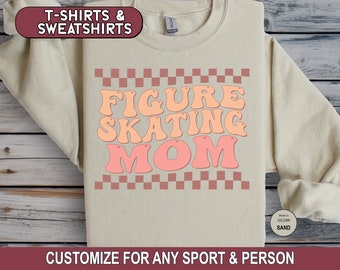 May include: A beige sweatshirt with a checkered pattern and the text "FIGURE SKATING MOM" in pink and orange letters.
