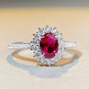 May include: A silver ring with a large oval ruby surrounded by a halo of smaller diamonds.