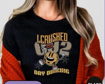 May include: Black t-shirt with the text "I CRUSHED 02 DAY DINKING" and a cartoon pickleball character. The design features a pickleball paddle and ball, with the word "T-SHIRTS" in a yellow box.