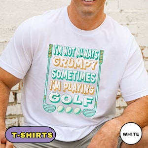 May include: White t-shirt with the text "I'M NOT ALWAYS GRUMPY SOMETIMES I'M PLAYING GOLF" in green, yellow, and blue. The design includes golf clubs and golf balls. The shirt is a crew neck.