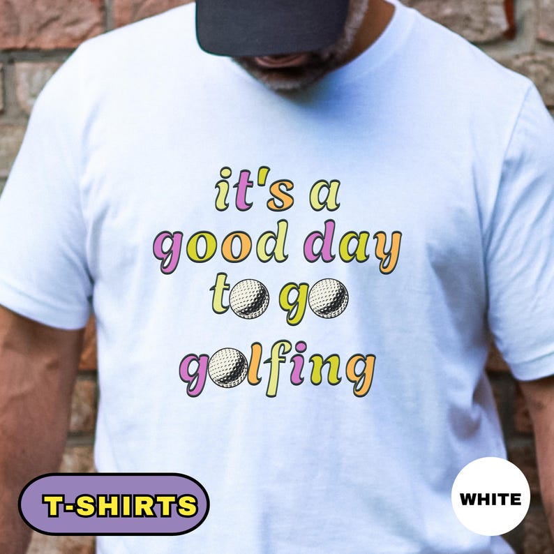May include: White t-shirt with the text "it's a good day to go golfing" in colorful lettering. The design includes golf balls. The shirt has a crew neck and short sleeves. The words "T-SHIRTS" and "WHITE" are also visible.