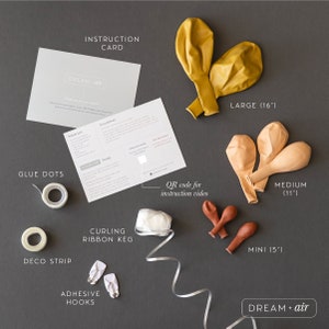May include: A set of balloon decorating supplies with instructions, including glue dots, deco strip, curling ribbon, adhesive hooks, and balloons in three sizes: 16 inches, 11 inches, and 5 inches. The balloons are yellow, peach, and brown. The instruction card includes the text "DREAM + air".