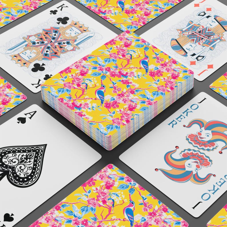 May include: A deck of playing cards with a floral design on the back. The deck features a yellow background with pink flowers and blue birds. Individual cards are visible, including the Ace of Spades, King of Clubs, and Joker.