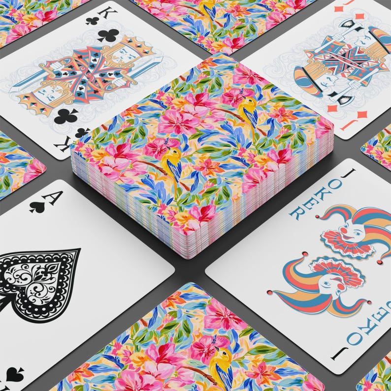 May include: A deck of playing cards with a floral design featuring pink flowers, blue leaves, and yellow birds. The deck is surrounded by individual cards, including the Ace of Spades, King of Clubs, and a Joker card.