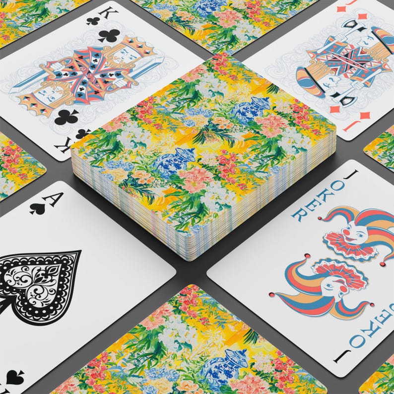May include: A deck of playing cards with a floral design on the back, featuring yellow, pink, blue, and green colors. The cards are arranged around a deck, with the Ace of Spades, King of Clubs, and Joker cards visible.