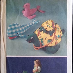 May include: Simplicity pattern featuring stuffed animal designs. Includes a pink seal, a blue and white checkered whale, and a turtle with a yellow shell. The pattern also shows a child with the turtle.