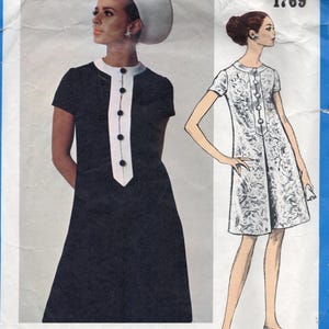 May include: Vintage Vogue Americana sewing pattern featuring two dress designs by Oscar de la Renta. One dress is navy with white trim and buttons, the other is a white floral print. The pattern number is 1769.