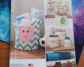 May include: A Simplicity sewing pattern for making storage containers. The pattern includes instructions for making a variety of containers, including a large container with a sheep face, a smaller container with a frog face, and a set of three wall-mounted containers. The pattern also includes a small soccer ball and a book titled "Toy Boat felia".