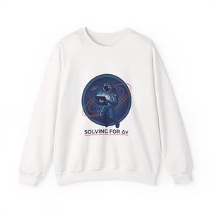May include: White crew neck sweatshirt with a graphic of an astronaut holding a laptop, set against a blue and orange space-themed background. The text "SOLVING FOR Δv" is printed below the graphic.