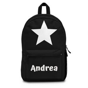 Pode incluir: Mochila preta com uma grande estrela branca na frente. A mochila tem um bolso frontal com zíper e o nome "Andrea" impresso em branco. Inclui uma alça superior e um bolso lateral de malha.