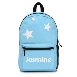 May include: A light blue backpack with white stars and the name "Jasmine" in white. The backpack has a black zipper, a black handle, and a black mesh side pocket. The bag is designed for carrying school supplies.