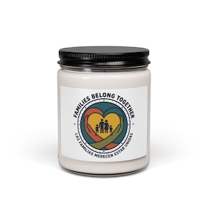 May include: A white jar candle with a black lid. The label features a heart-shaped design with a family silhouette, hands, and the text "FAMILIES BELONG TOGETHER" and "LAS FAMILIAS MERECEN ESTAR UNIDAS".