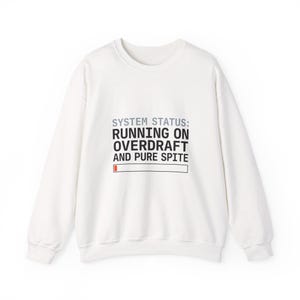 Könnte beinhalten: Weißes Sweatshirt mit Rundhalsausschnitt und dem Text "SYSTEM STATUS: RUNNING ON OVERDRAFT AND PURE SPITE" in Schwarz. Das Design beinhaltet eine Ladebalken-Grafik. Es ist ein lässiges Unisex-Kleidungsstück.