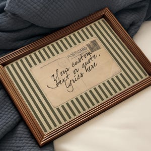 Op de afbeelding: Een ingelijste ansichtkaart met een bruine houten lijst. De ansichtkaart heeft een gestreepte achtergrond, een vintage postzegel en de tekst "Your custom text or quote. Lyrics here."