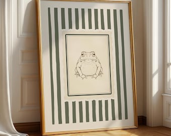 May include: A framed art print featuring a detailed line drawing of a frog. The artwork is set against a cream-colored background with a green and white striped border, encased in a gold frame. The print is leaning against a white wall.
