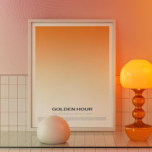May include: A framed print with an orange gradient and the text "GOLDEN HOUR" sits on a glass shelf. A white, egg-shaped sculpture and a retro-style lamp with a round, yellow shade and a brown base are also on the shelf. The background is a pink and orange wall.