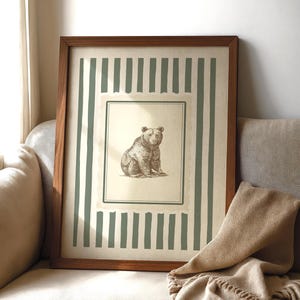 May include: A framed art print featuring a detailed sepia-toned illustration of a bear. The artwork is set against a cream background with vertical green stripes and a brown wooden frame. The print is displayed on a beige sofa.
