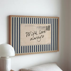 Może przedstawiać: Oprawiona grafika z motywem vintage pocztówki z napisem "With love always" w ozdobnym kroju pisma. Pocztówka umieszczona jest na tle w niebiesko-białe paski, w jasnej drewnianej ramie.