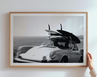 Könnte beinhalten: Schwarz-Weiß-Druck in einem Rahmen mit einem Oldtimer und Surfbrettern auf dem Dach. Das Auto fährt in der Nähe des Ozeans. Das Bild befindet sich in einem Holzrahmen.