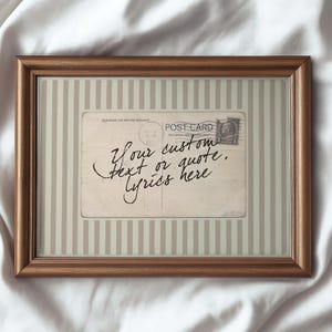 Puede incluir: Una impresión enmarcada de postal con un marco de madera marrón. La postal tiene una estética vintage con el texto "Your custom text or quote, lyrics here" en cursiva. El fondo presenta rayas verticales.