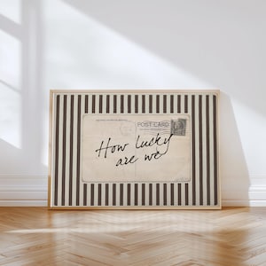 Framed vintage-style digital art featuring a sepia-toned postcard with the handwritten phrase “How lucky are we.” The postcard is set against a background of vertical brown stripes, adding a graphic yet nostalgic look. Perfect for gallery walls, vintage-inspired interiors, or thoughtful gifts.