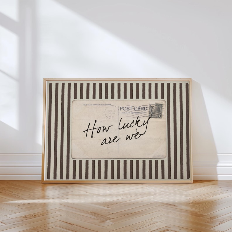 Framed vintage-style digital art featuring a sepia-toned postcard with the handwritten phrase “How lucky are we.” The postcard is set against a background of vertical brown stripes, adding a graphic yet nostalgic look. Perfect for gallery walls, vintage-inspired interiors, or thoughtful gifts.