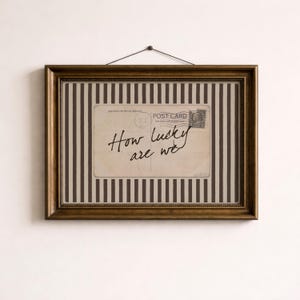 Framed vintage-style digital art featuring a sepia-toned postcard with the handwritten phrase “How lucky are we.” The postcard is set against a background of vertical brown stripes, adding a graphic yet nostalgic look. Perfect for gallery walls, vintage-inspired interiors, or thoughtful gifts.