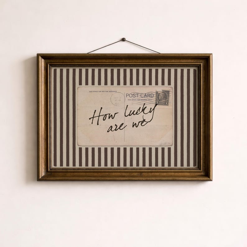 Framed vintage-style digital art featuring a sepia-toned postcard with the handwritten phrase “How lucky are we.” The postcard is set against a background of vertical brown stripes, adding a graphic yet nostalgic look. Perfect for gallery walls, vintage-inspired interiors, or thoughtful gifts.