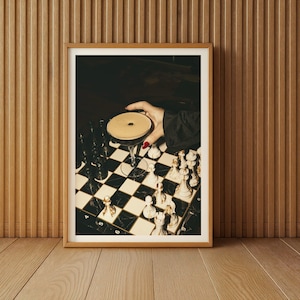 Moody photograph of a hand with red nails holding a martini over a chessboard, dramatic bar and game night themed wall art, printable decor