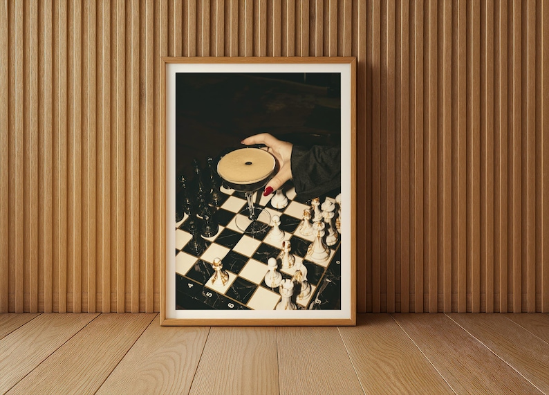 Moody photograph of a hand with red nails holding a martini over a chessboard, dramatic bar and game night themed wall art, printable decor