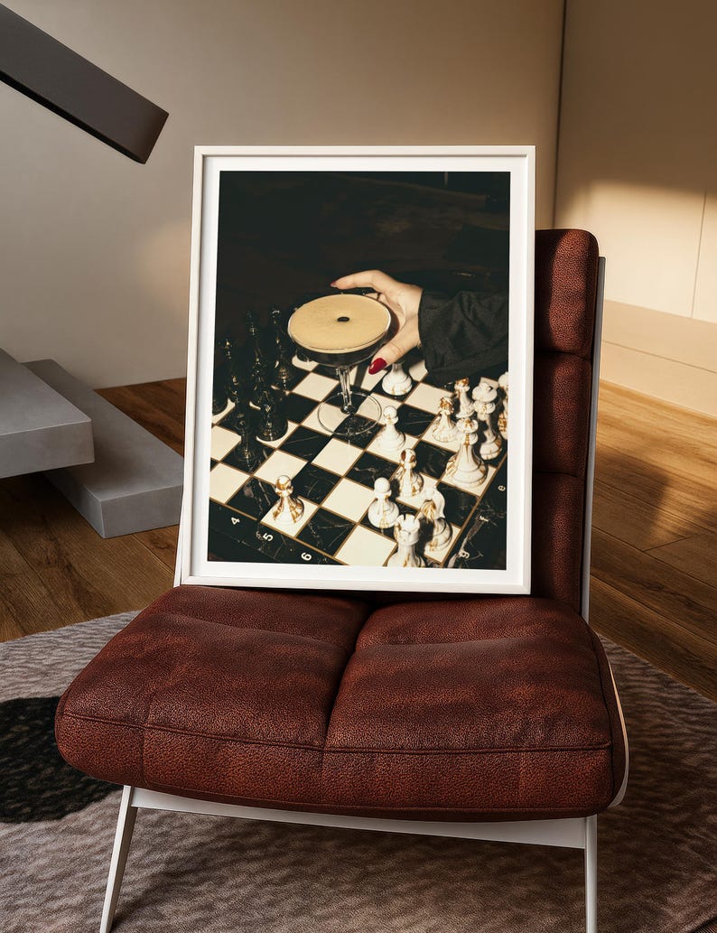 Moody photograph of a hand with red nails holding a martini over a chessboard, dramatic bar and game night themed wall art, printable decor
