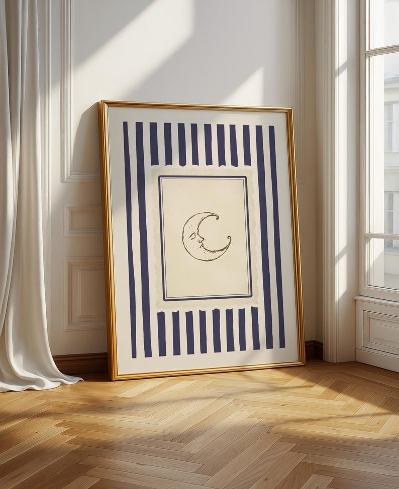 Vintage-inspired printable wall art featuring a hand-drawn crescent moon illustration with a softly smiling face, centered within a muted parchment-style frame. The moon is surrounded by layered, scalloped-edge borders and encased in deep navy vertical stripes, adding a celestial yet refined aesthetic. Styled in a minimalist, quiet luxury interior with warm wood flooring and decorative wall paneling, this digital download evokes dreamy, moody nighttime vibes.