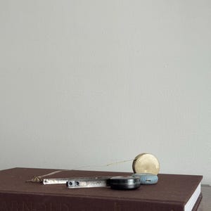 Może przedstawiać: Brązowa książka z napisem "ARNOLD" na grzbiecie. Srebrna składana linijka, czarna miarka, złoto-niebieska miarka i mały złoty przedmiot leżą na książce.